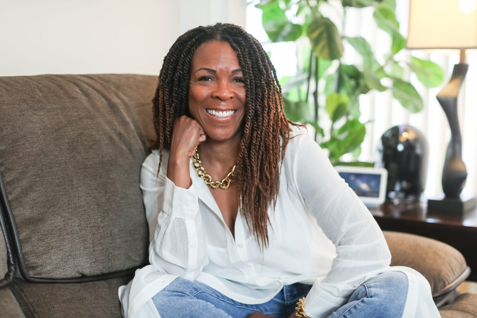 A woman sitting on top of a couch with her hands under the chin.