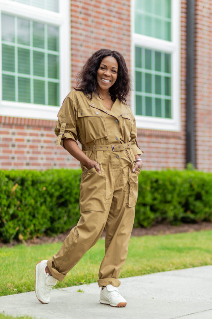 Person in tan jumpsuit standing by brick building