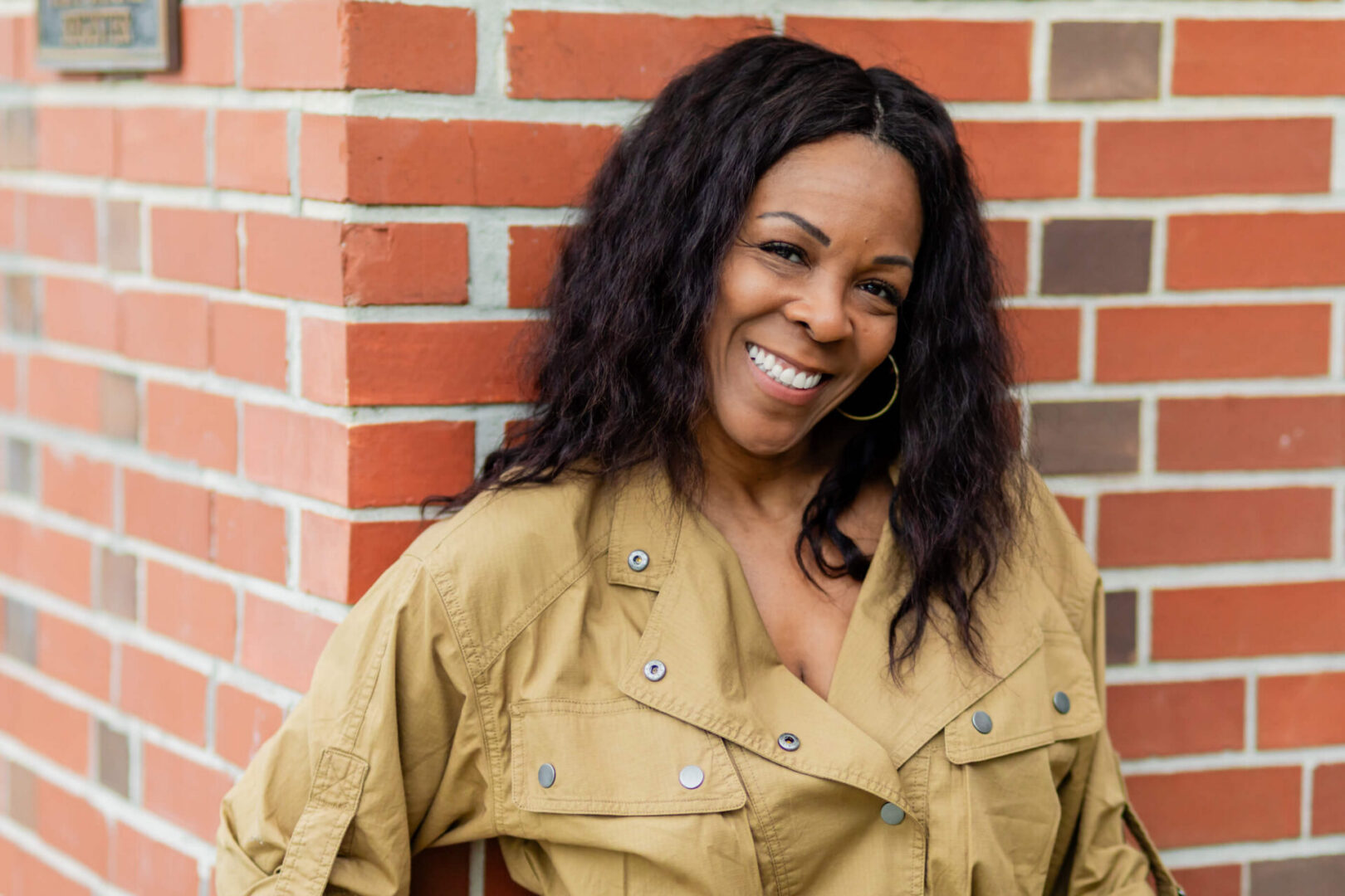 Woman leaning against brick corner, smiling warmly