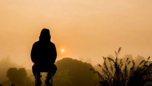 Hooded figure seated before misty golden sunrise